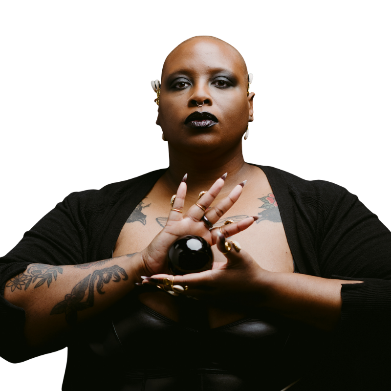 Ensoulment Doula Samar exudes confidence and power with their tattoos, obsidian orb, and all-black ensemble.